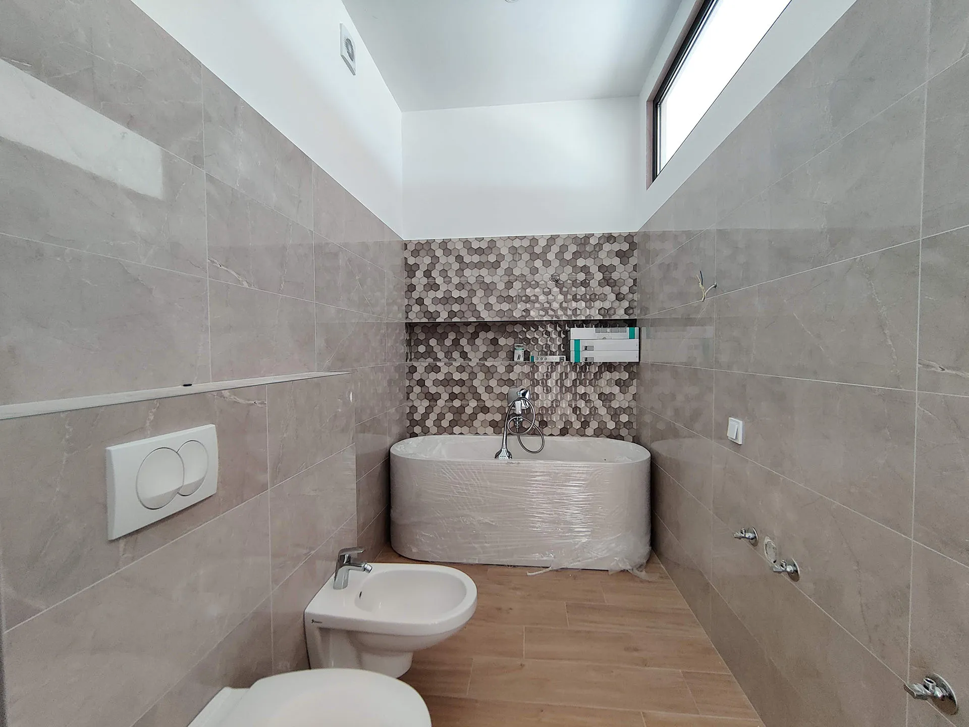 Modernes Badezimmer in einer Wohnung in Bečići, Montenegro: neue Badewanne, Bidet, Marmoroptik-Fliesen und Mosaikverkleidung.