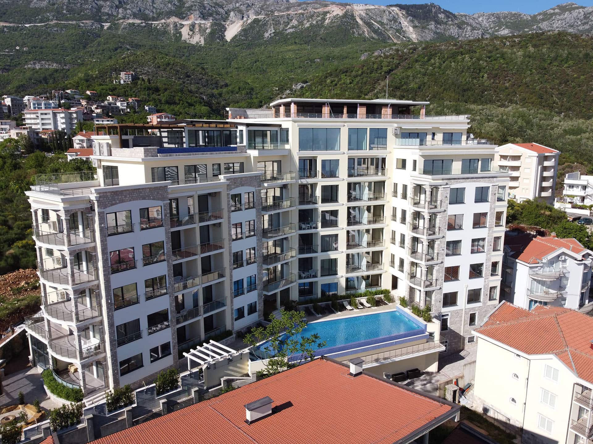 Modern residential complex with a pool in Bečići, Montenegro: view of the building with panoramic windows and mountains.