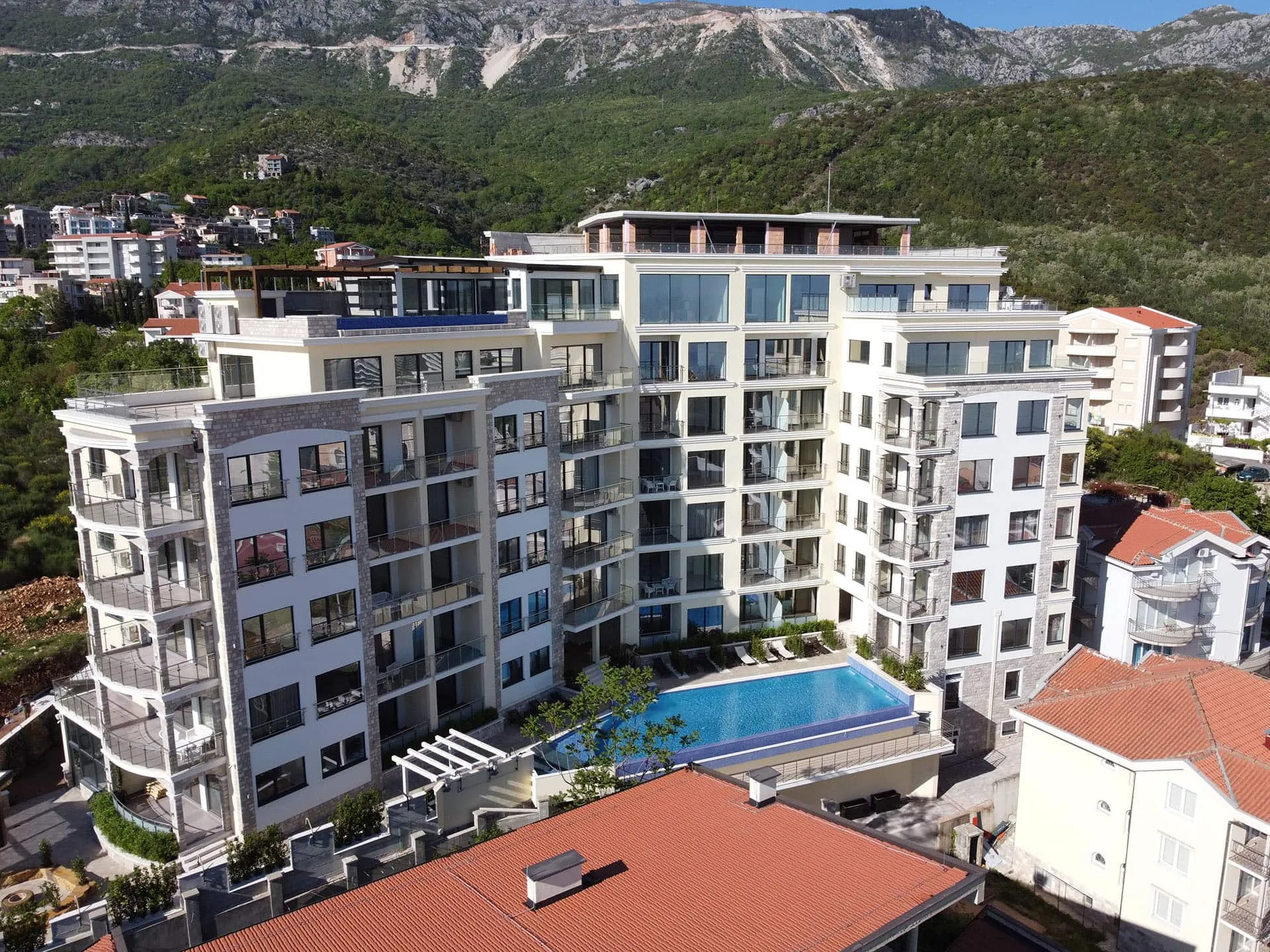 Moderner Wohnkomplex mit Pool in Bečići, Montenegro: Blick auf das Gebäude mit Panoramafenstern und Bergen.