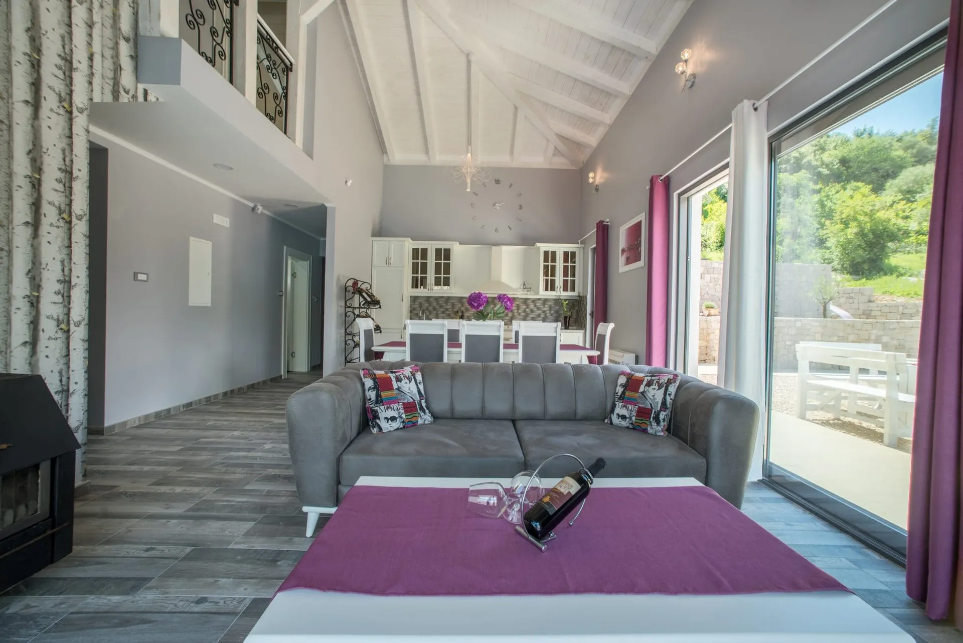 Modernes Wohnzimmer mit grauem Sofa, Couchtisch, offener Küche im Hintergrund und großem Fenster.