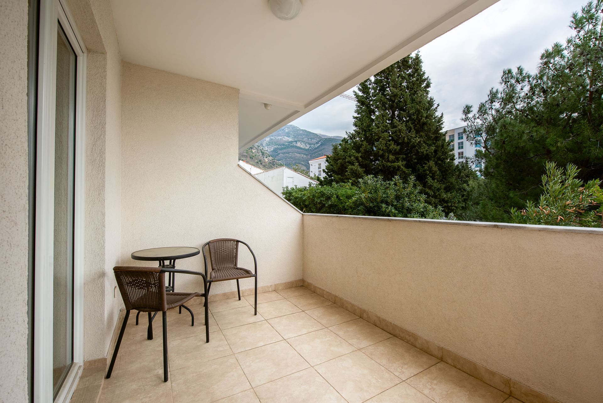 Gemütlicher Balkon mit Rattanmöbeln und Bergblick in einer Wohnung in Bečići, Montenegro. Fliesenboden, helle Ausstattung.