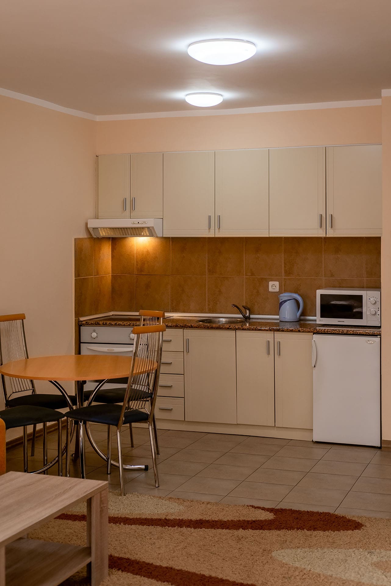 Küche in einer Wohnung in Bečići, Montenegro: helle Einbauküche, Esstisch, Einbaugeräte und gefliester Spritzschutz.