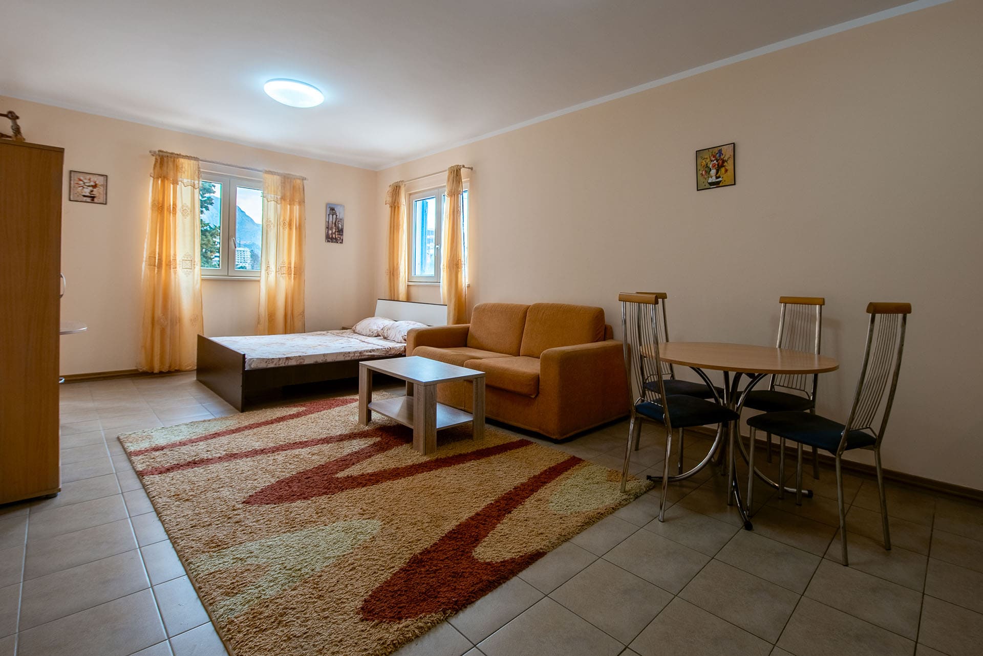 Wohnzimmer in einer Wohnung in Bečići, Montenegro: Doppelbett, orangefarbenes Sofa, Esstisch und Fliesenboden.