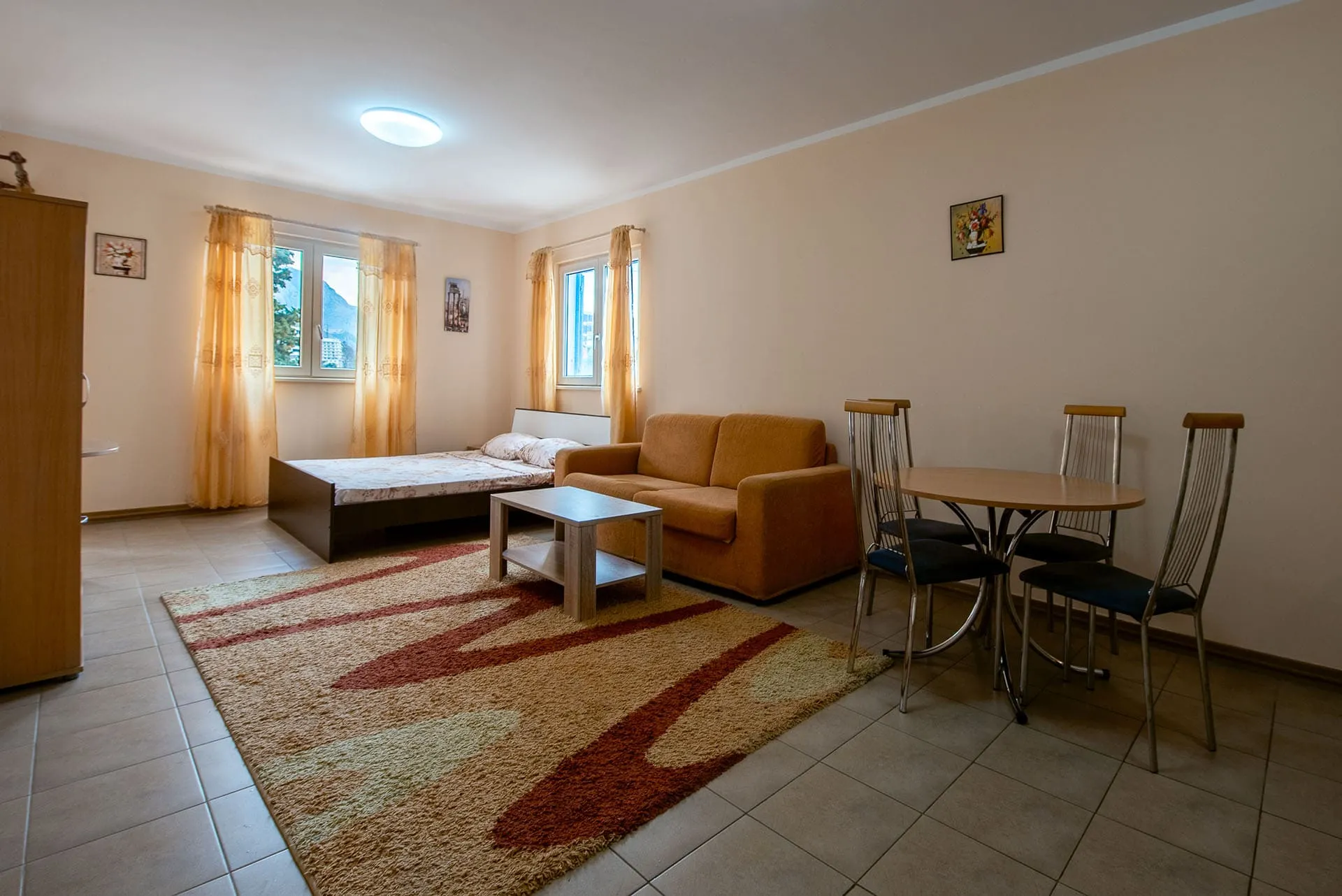 Комната с кроватью, диваном, обеденным столом и шкафом на tiled полу.