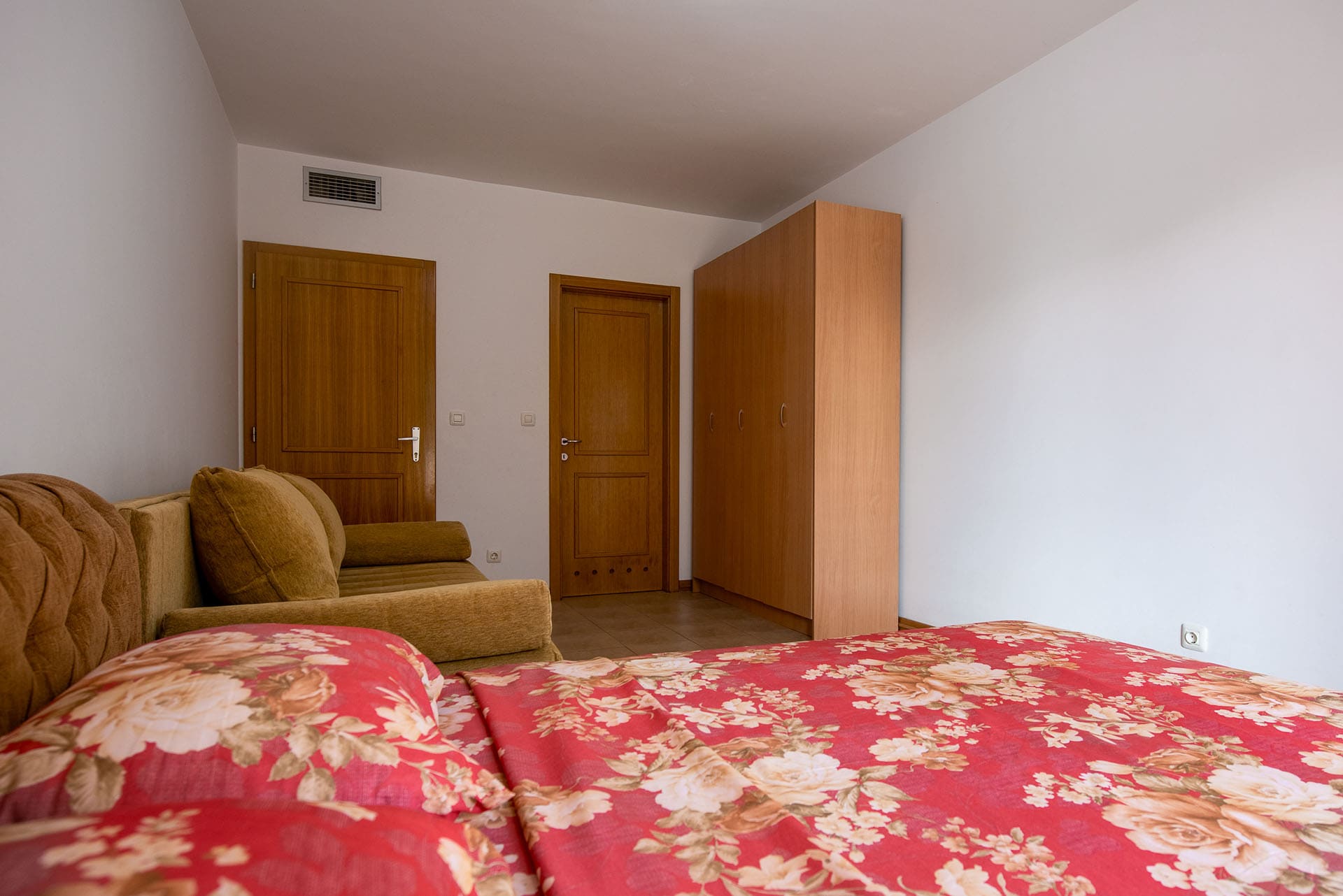 Schlafzimmer in einer Wohnung in Bečići, Montenegro: Doppelbett, weiches Sofa, Kleiderschrank und Holztüren im Innenbereich.