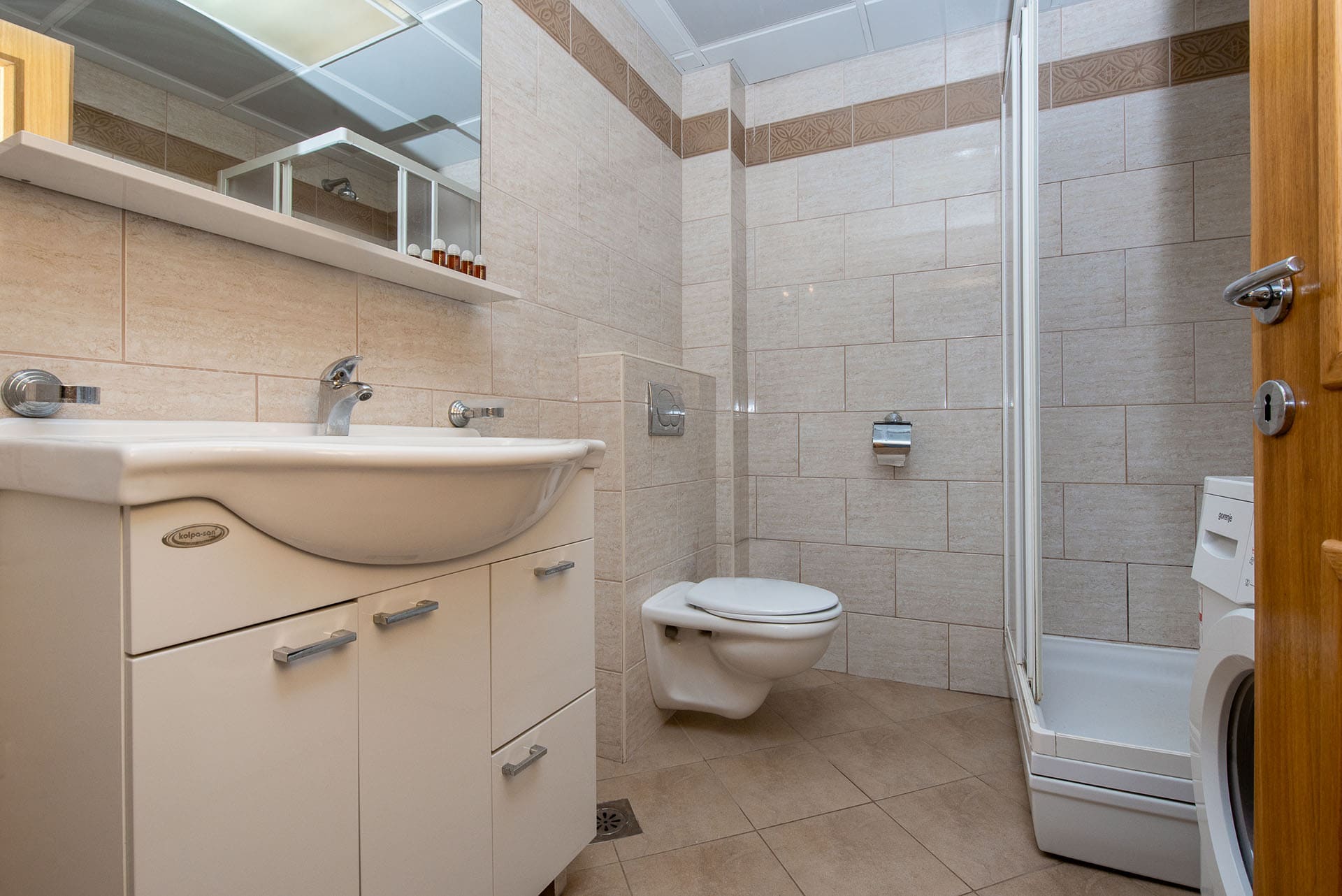 Badezimmer in einer Wohnung in Bečići, Montenegro: Duschkabine, Hänge-WC, Waschtischunterschrank und helle Fliesen.