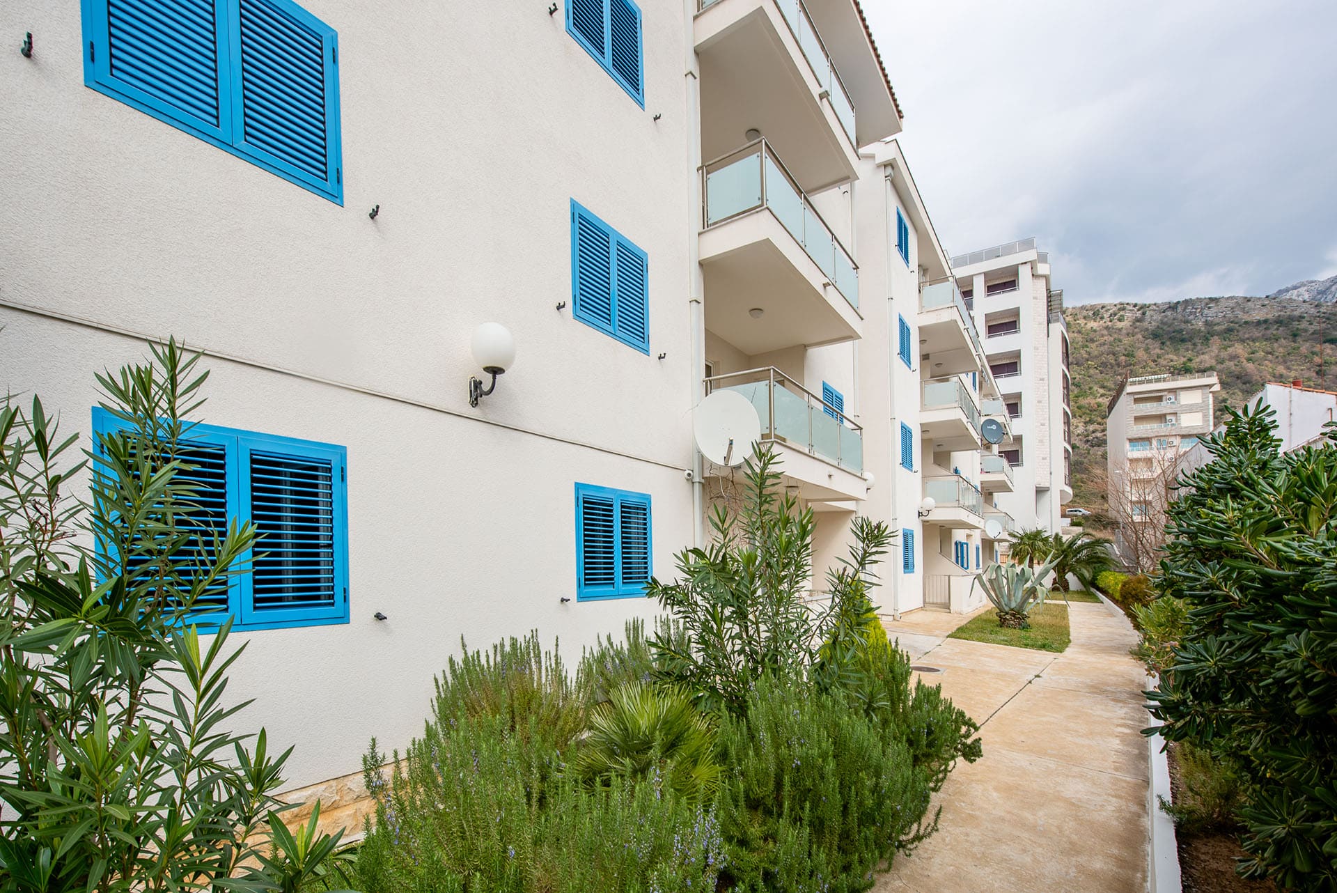 Fassade eines modernen Wohnhauses mit blauen Fensterläden und Balkonen in Bečići, Montenegro, Blick auf das Grundstück.