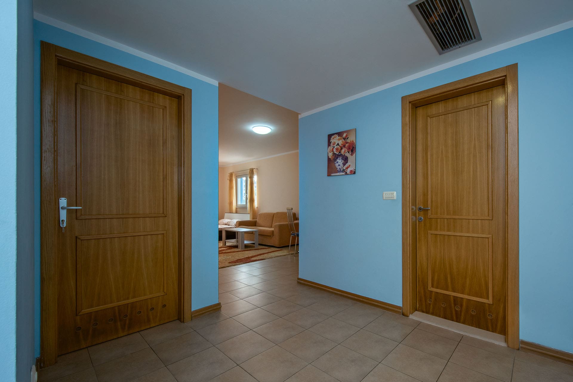 Flur mit blauen Wänden und Holztüren in einer Wohnung, Bečići, Montenegro, Blick ins Wohnzimmer mit Möbeln.