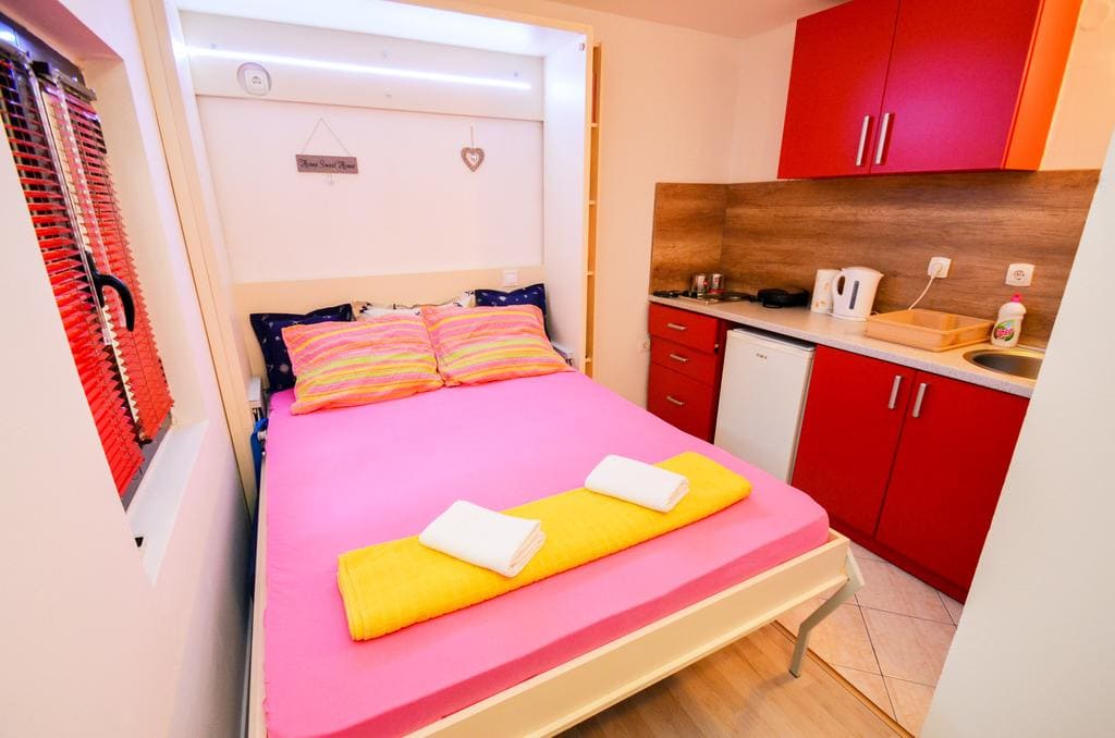 Schlafzimmer mit Doppelbett und Küchenzeile in einem Haus in Kotor, Montenegro. Modernes Interieur mit roten Möbeln.