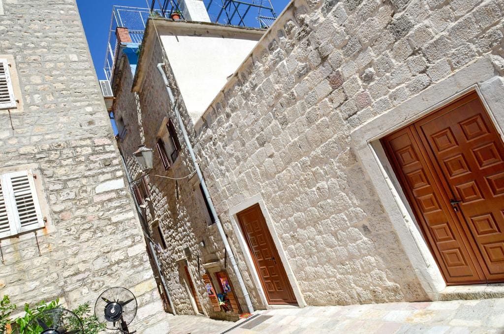 Enge Gasse in der Altstadt von Kotor, Montenegro: traditionelle Steinhäuser mit Holztüren und weißen Fensterläden.