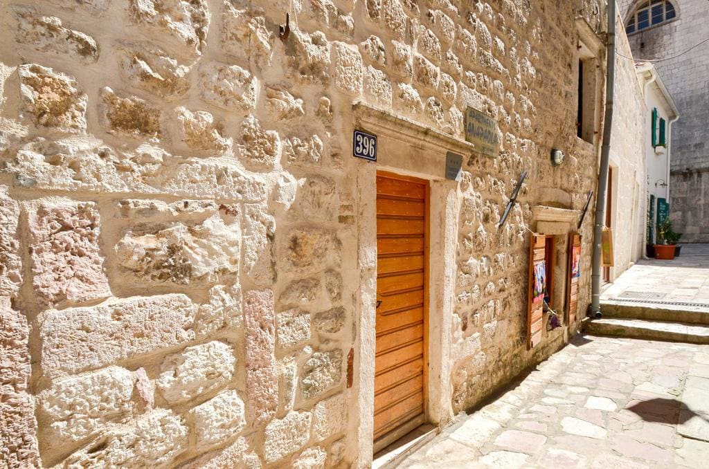 Fassade eines alten Steinhauses im historischen Zentrum von Kotor, Montenegro, mit Holztür und Kopfsteinpflaster.