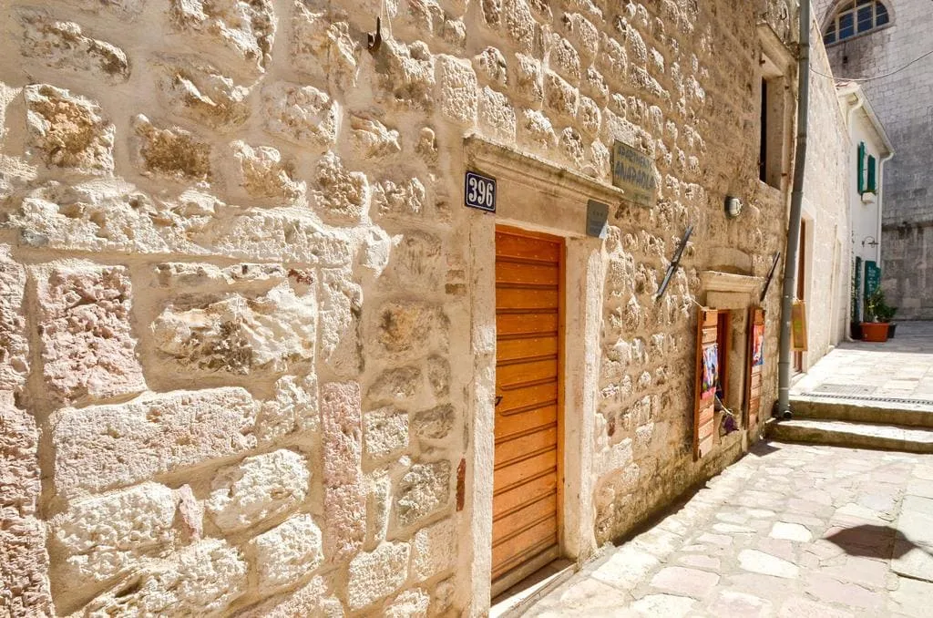 Facade of an old stone house in the historic center of Kotor, Montenegro, with a wooden door and cobblestone paving.