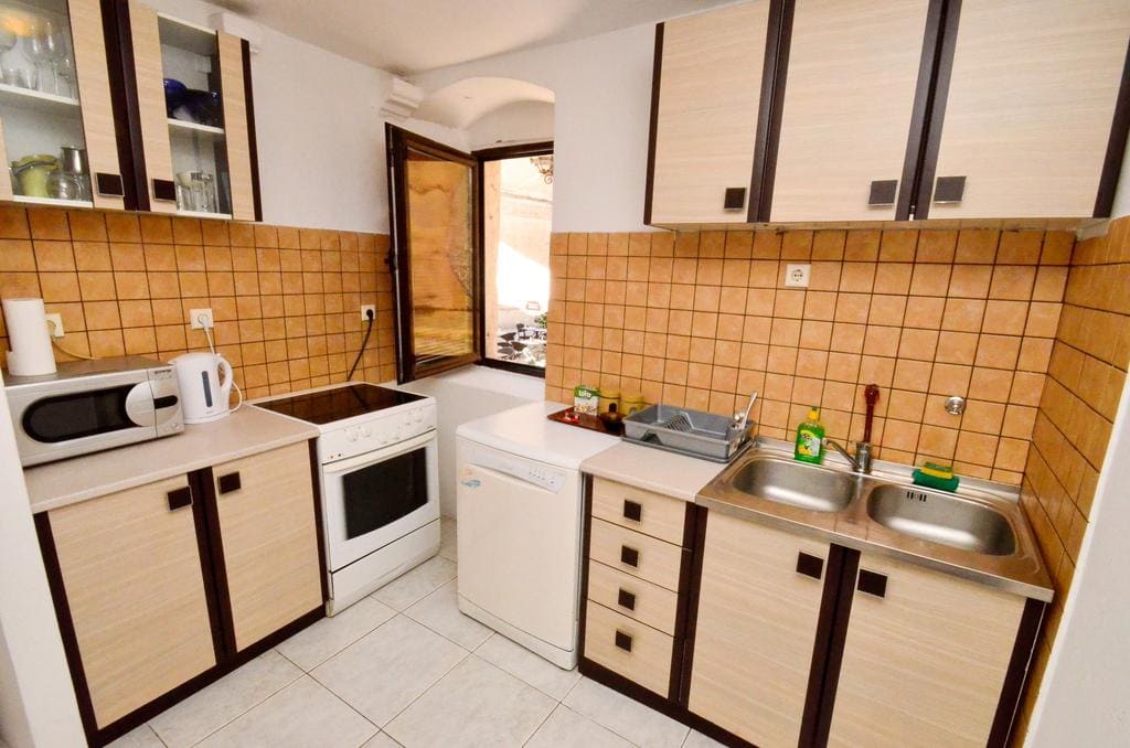 Helle Küche in einem Haus in Kotor, Montenegro: beige Einbauküche, Fliesenspiegel, Spüle und Haushaltsgeräte.