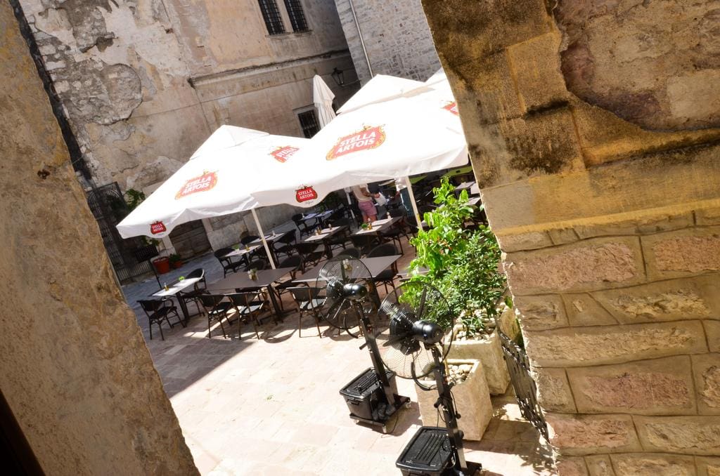 Gemütliche Restaurantterrasse in der Altstadt von Kotor, Montenegro: Tische unter Sonnenschirmen und steinerne Architektur der Gebäude.