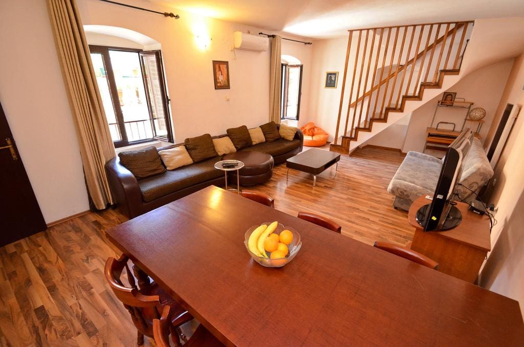 Wohnzimmer mit Holztreppe und Essbereich in einem Haus in Kotor, Montenegro: Ledersofa und Parkettboden.