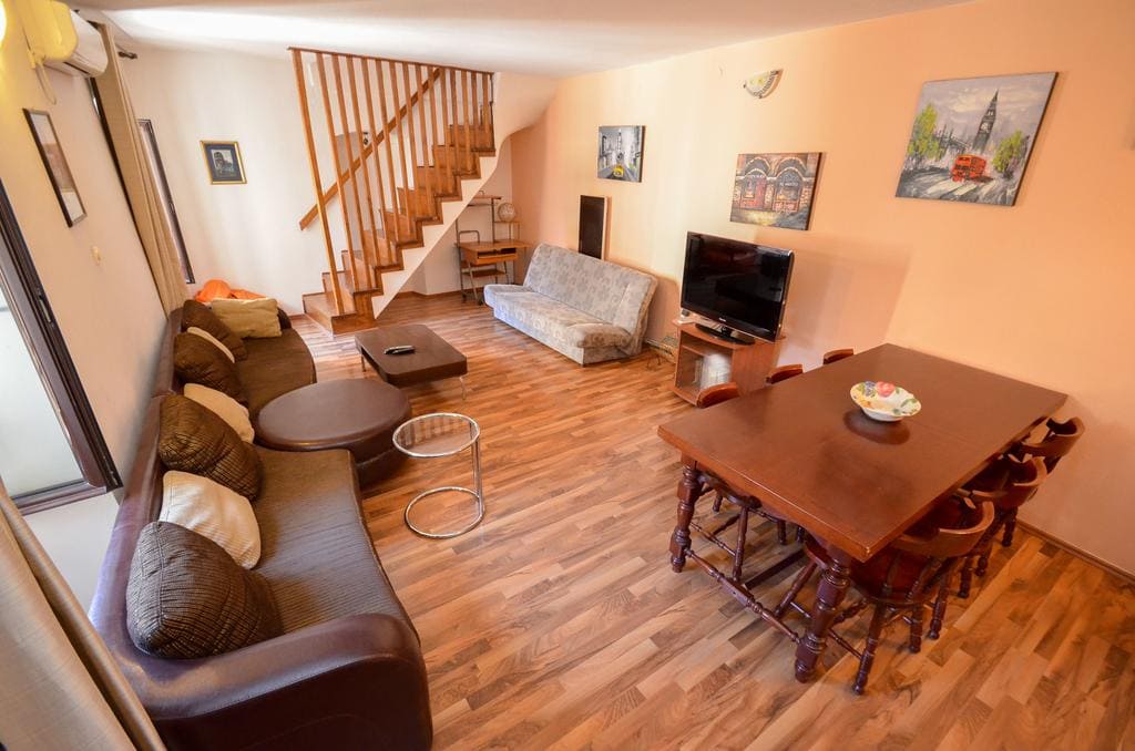 Wohnzimmer mit Holztreppe und Essbereich in einem Haus in Kotor, Montenegro: Polstermöbel, TV und Parkettboden.