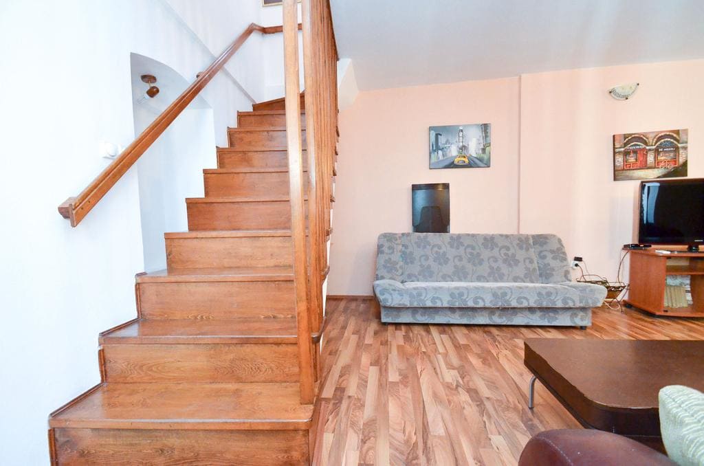 Wohnzimmer mit Holztreppe und Polstermöbeln im Haus, Stadt Kotor, Montenegro. Innenraum mit Laminat und TV-Bereich.