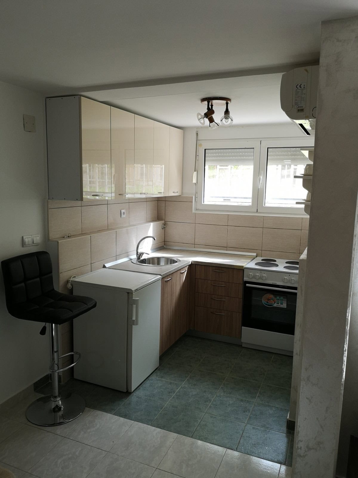 Kompakte Küche in einer Wohnung in Budva, Montenegro: helle Küchenzeile, Herd, Kühlschrank und Barhocker im Interieur.