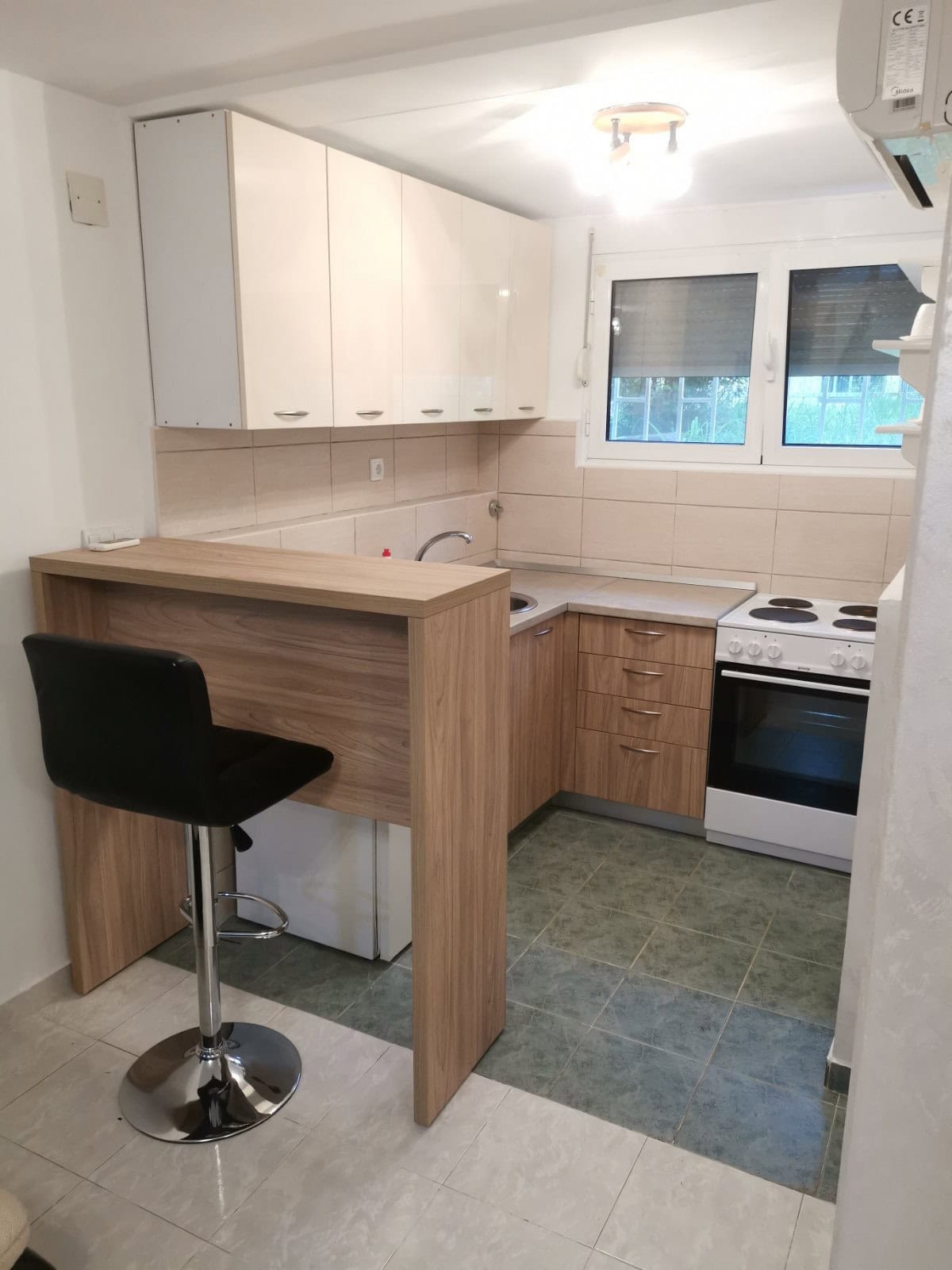 Kompakte Küche in einer Wohnung in Budva, Montenegro: helle Einbauküche, Bartheke, Herd und Fliesenboden.