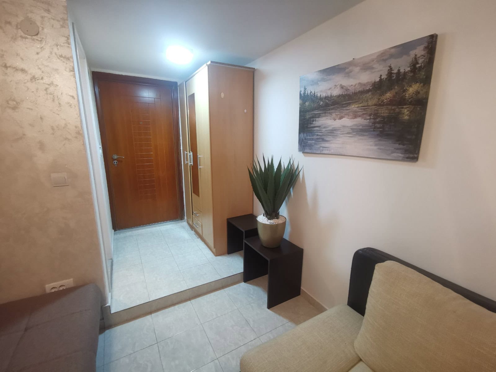 Flur in einer Wohnung in Budva, Montenegro: helle Gestaltung, Holzschrank, Fliesenboden und Dekor mit einem Bild.