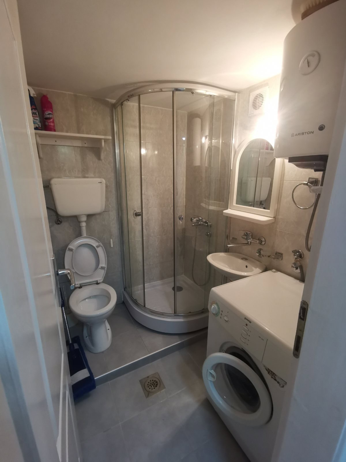 Badezimmer in einer Wohnung in Budva, Montenegro: Duschkabine, Waschmaschine, Boiler und helle Fliesen.