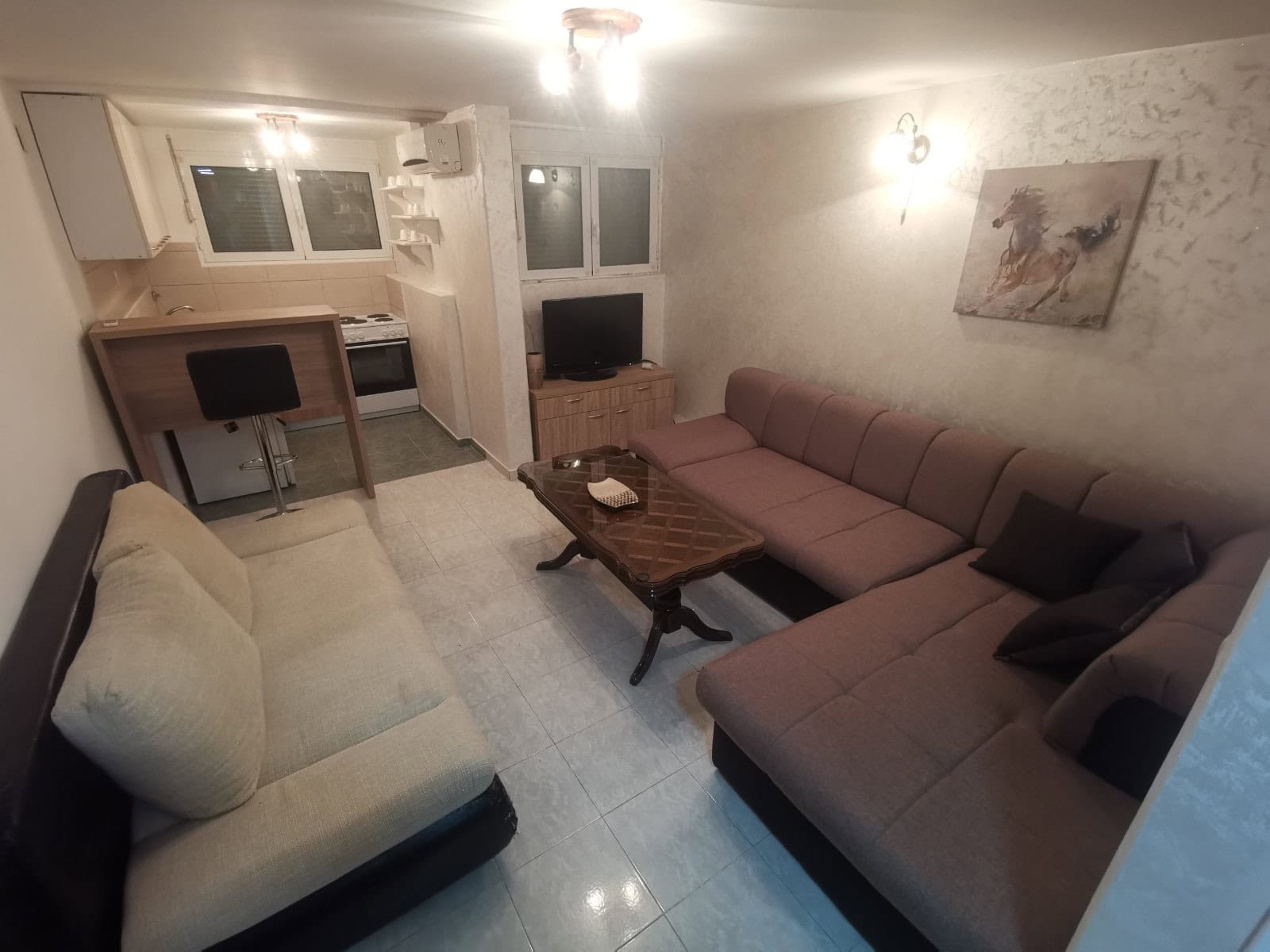Wohnzimmer mit Küche in einer Wohnung in Budva, Montenegro: Ecksofa, Essbereich, helle Ausstattung und Fliesenboden.