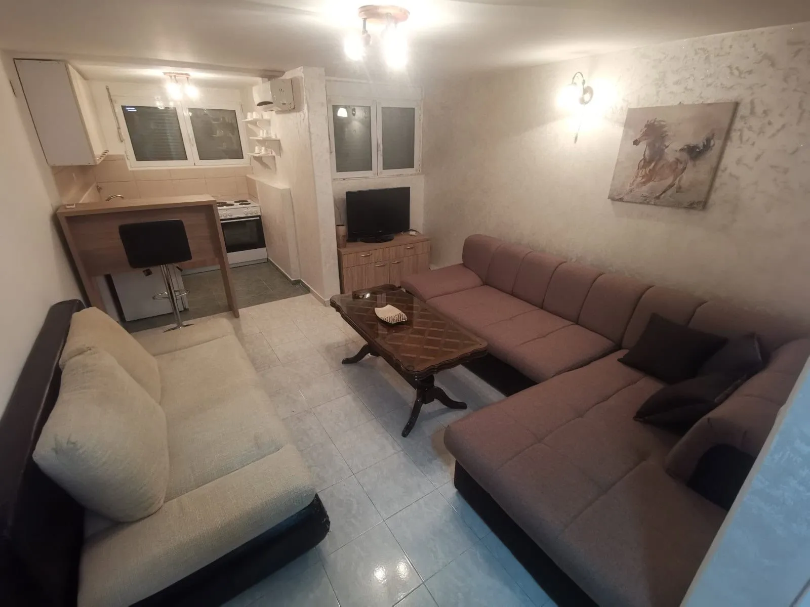 Salon z kuchnią w mieszkaniu w Budvie, Czarnogóra: narożna sofa, jadalnia, jasne wykończenie i podłoga z płytek.