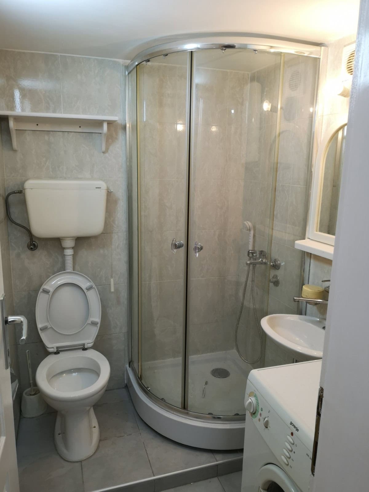 Badezimmer in einer Wohnung in Budva, Montenegro: Duschkabine, Sanitäranlagen und Waschmaschine in heller Ausführung.
