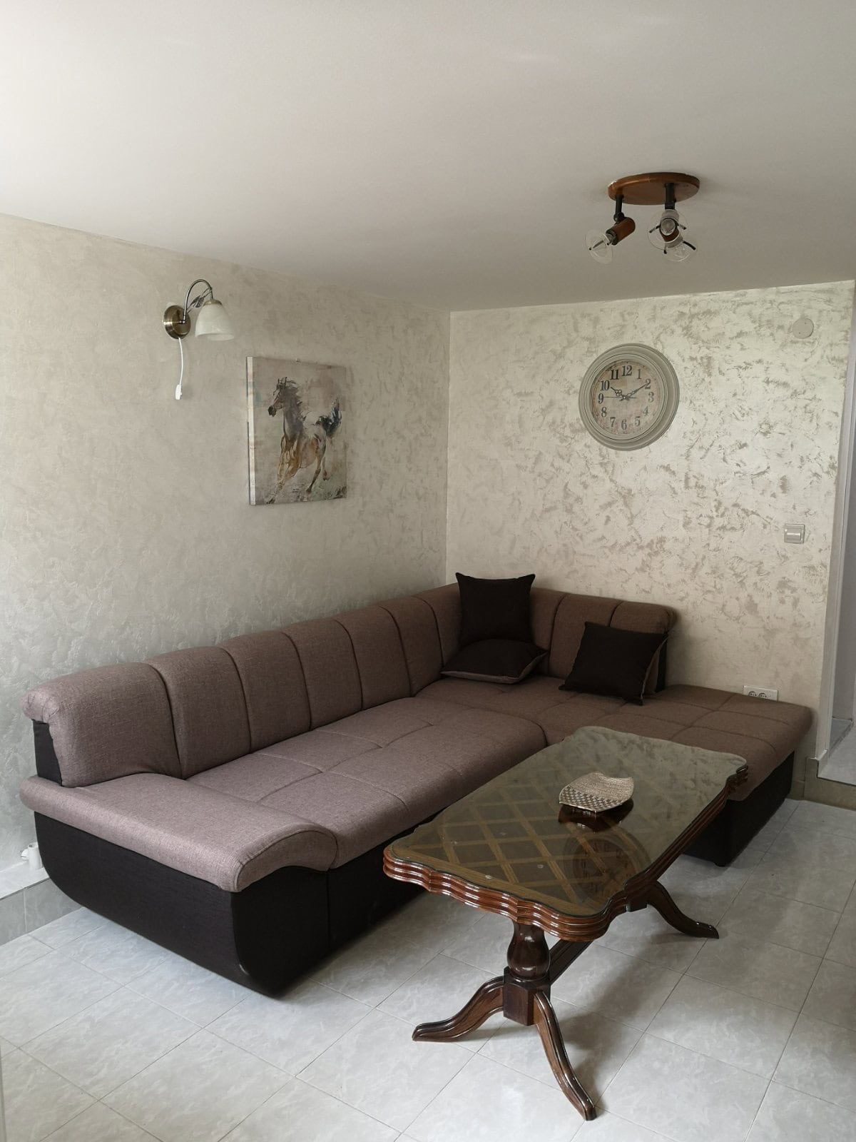 Gemütliches Wohnzimmer mit Ecksofa und Glastisch in einer Wohnung, Budva, Montenegro. Helle Wände, Dekor und Beleuchtung.