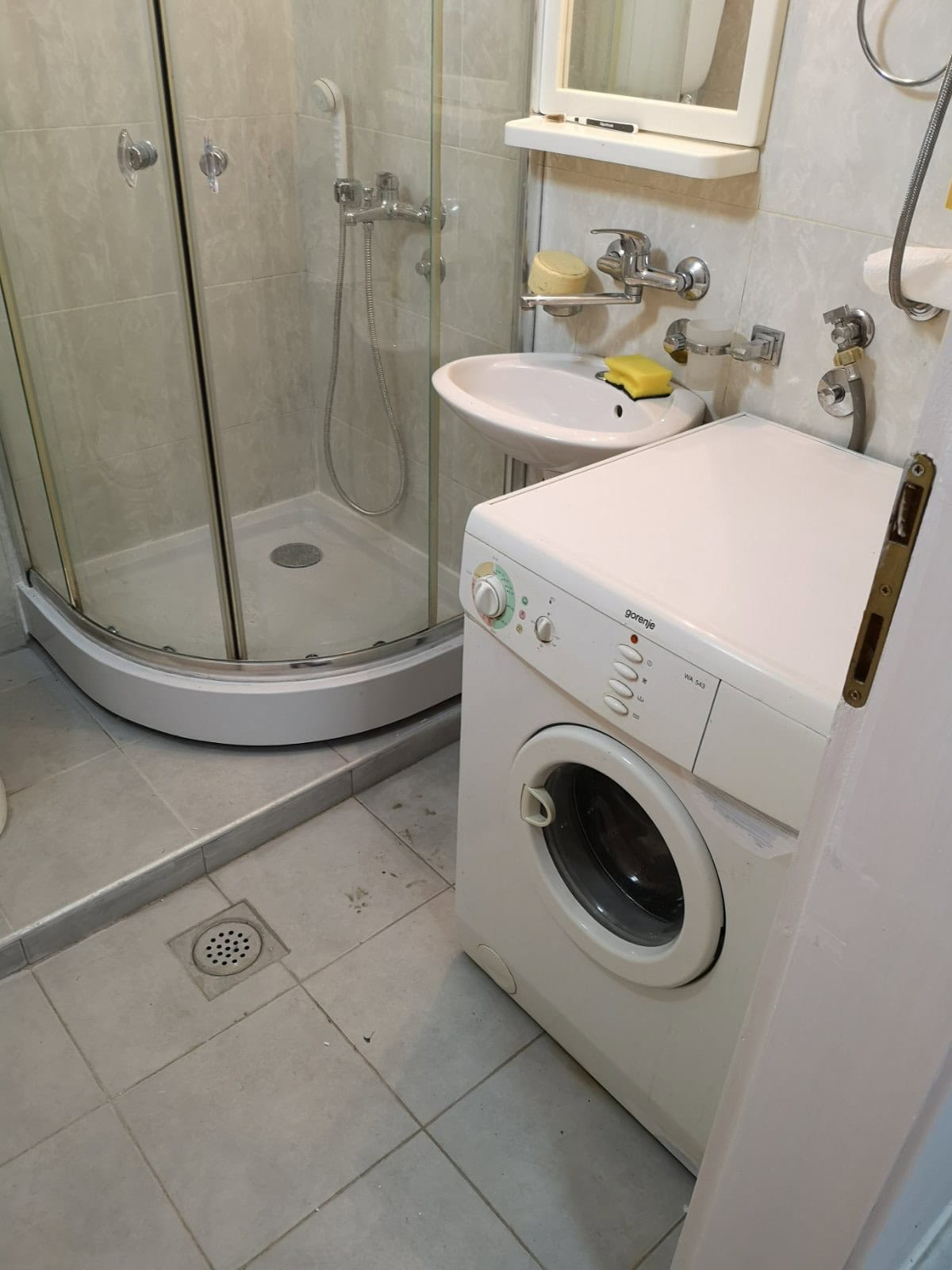 Badezimmer in einer Wohnung in Budva, Montenegro: Duschkabine, Waschbecken und Gorenje-Waschmaschine im Innenraum.