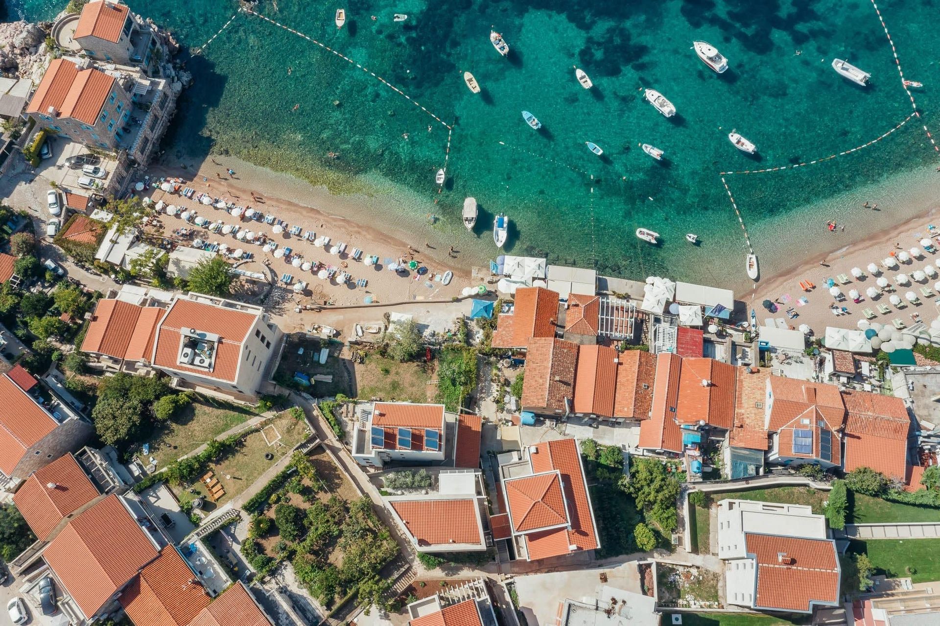 Aerial view of villas with tiled roofs and a beach with boats in Pržno, Montenegro. Seaside property.