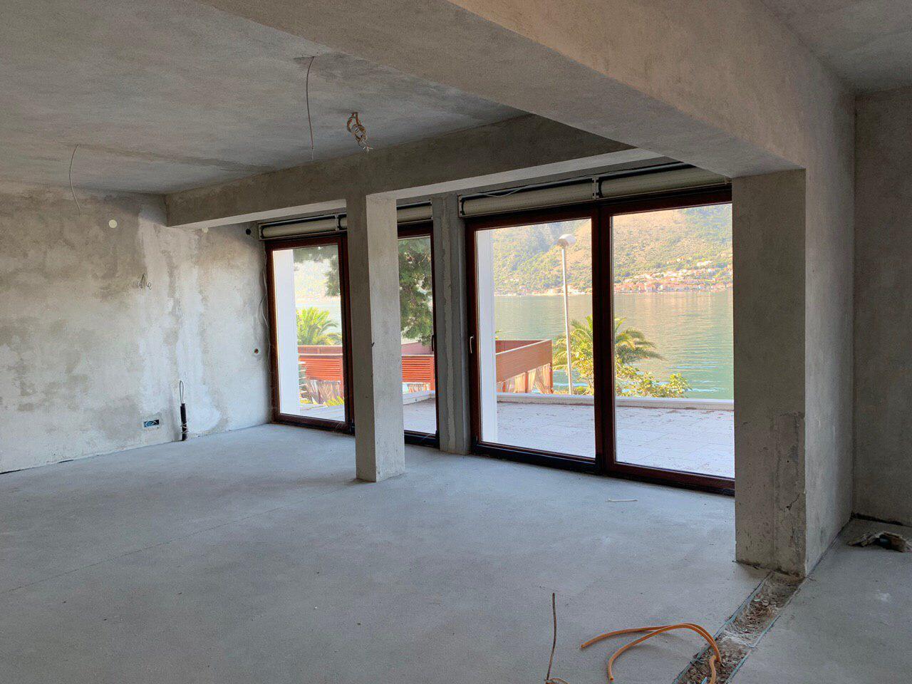Dnevna soba bez završne obrade u vili u izgradnji u Dobroti, Crna Gora, sa panoramskim pogledom na more i planine preko terase.