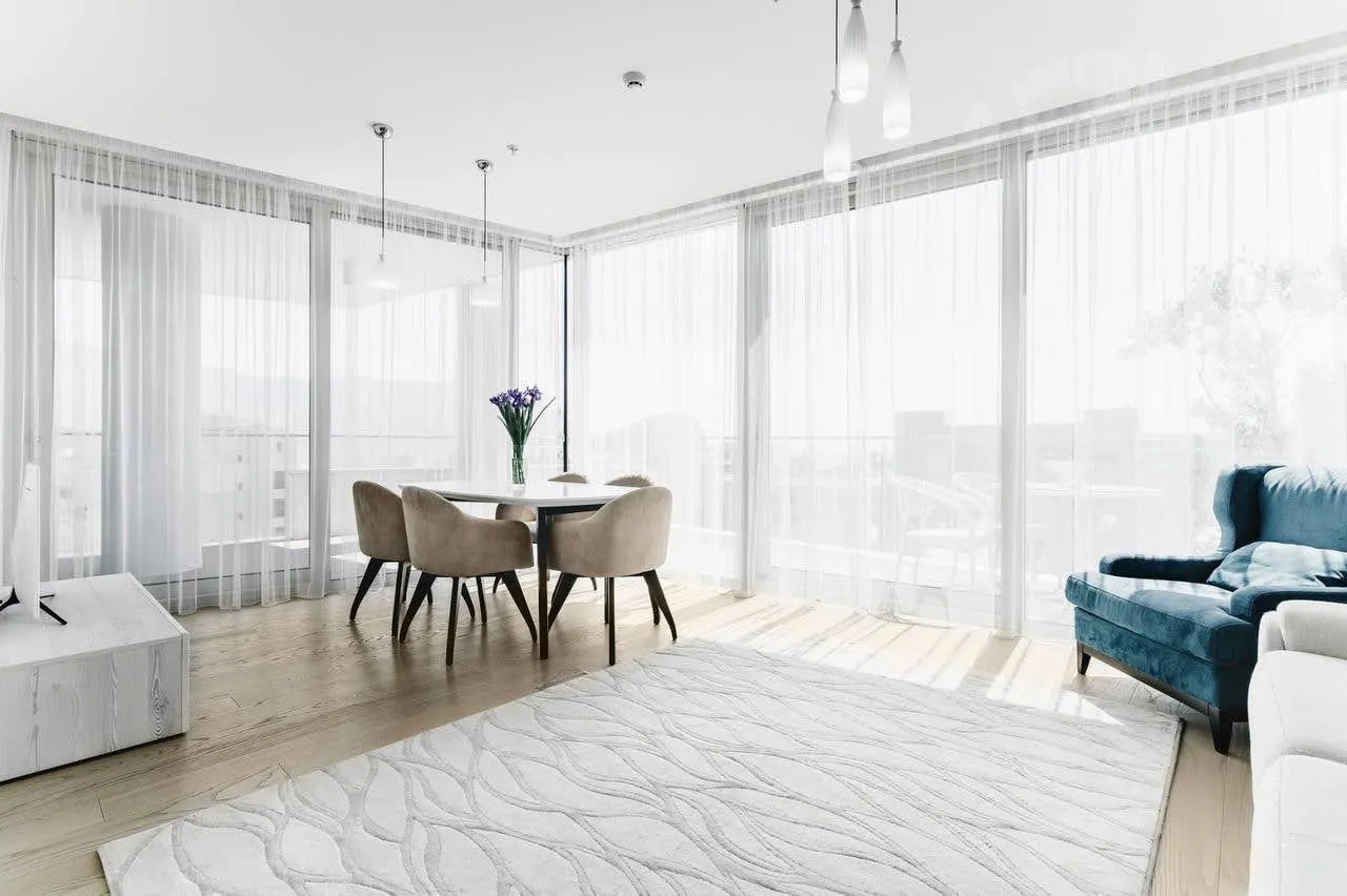 Helles Wohnzimmer in einer Wohnung in Budva, Montenegro: Panoramafenster, Essbereich, blauer Sessel und modernes Design.