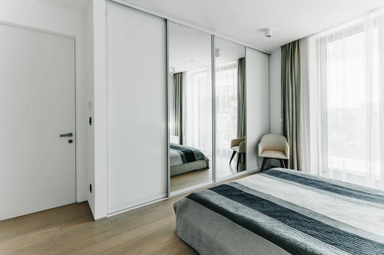 Modernes Schlafzimmer mit Spiegel-Schiebetürenschrank in einer Wohnung in Budva, Montenegro: helles Interieur, Panoramafenster.