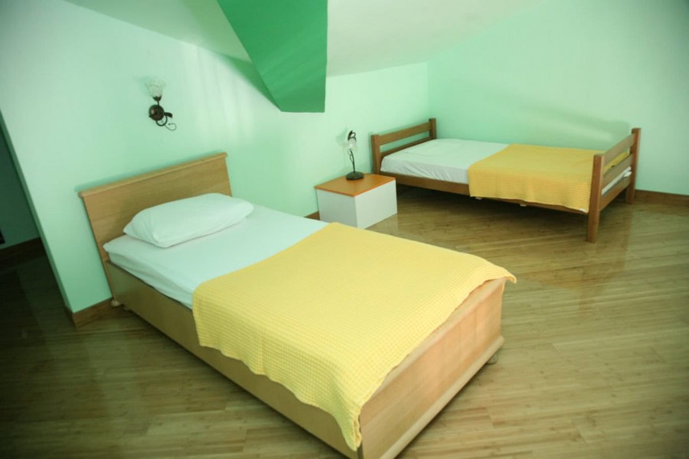 Schlafzimmer mit zwei Betten im Dachgeschoss einer Villa in Tivat, Montenegro: helle Wände, Holzmöbel und Holzboden.
