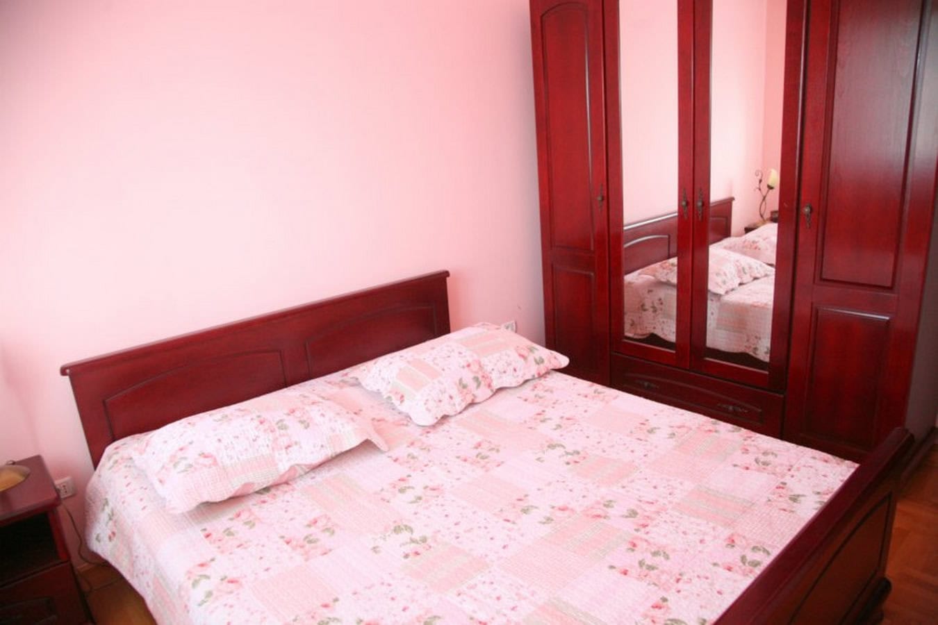 Schlafzimmer in einer Villa in Tivat, Montenegro: Doppelbett und Kleiderschrank aus dunklem Holz, rosa Wände, gemütliches Interieur.