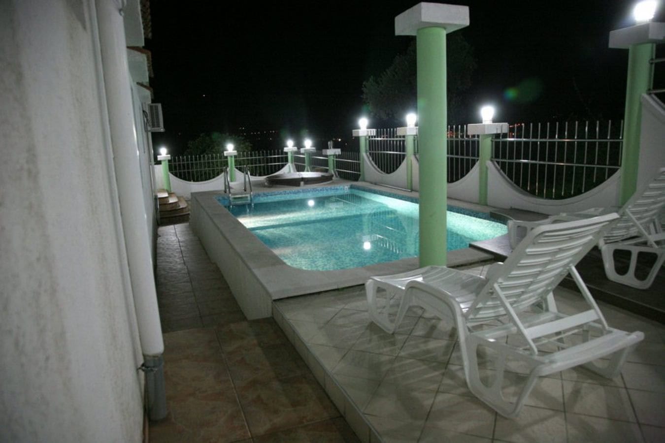 Offener Pool mit Beleuchtung und Liegestühlen auf der Terrasse der Villa in Tivat, Montenegro, Nachtansicht.
