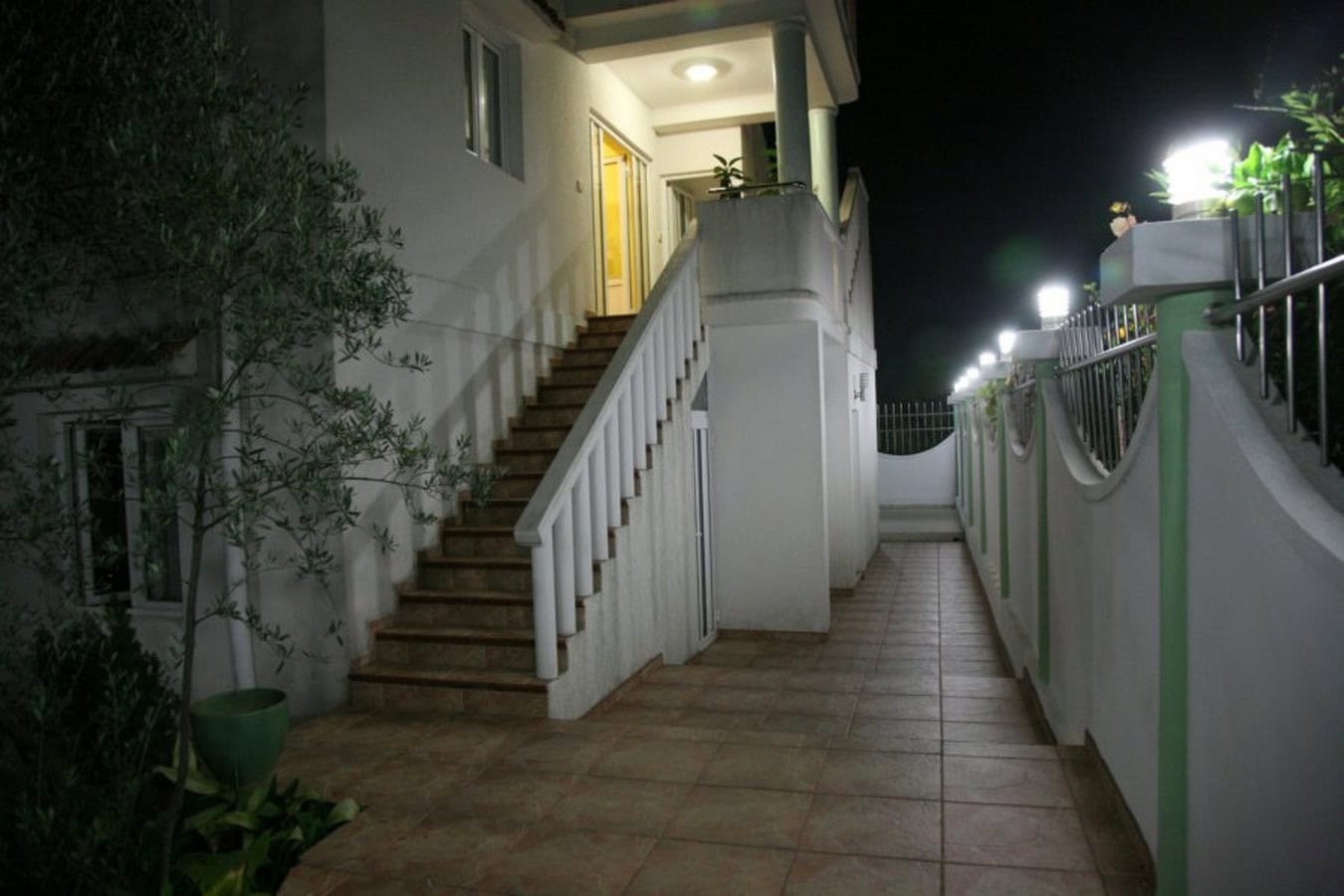 Abendansicht der Fassade einer Villa in Tivat, Montenegro: Außentreppe, beleuchtete Terrasse und gepflegtes Grundstück.