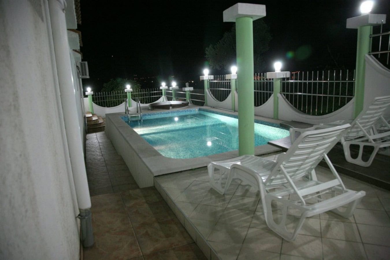 Offener Pool mit Beleuchtung und Liegestühlen auf der Terrasse der Villa in Tivat, Montenegro, Nachtansicht.