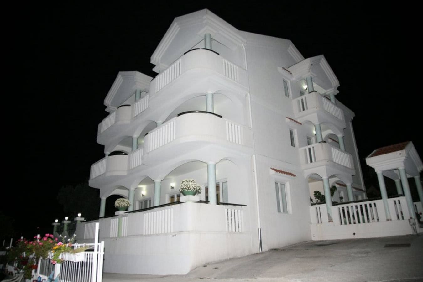 Dreistöckige weiße Villa in Tivat, Montenegro, mit offenen Balkonen und nächtlicher Fassadenbeleuchtung.