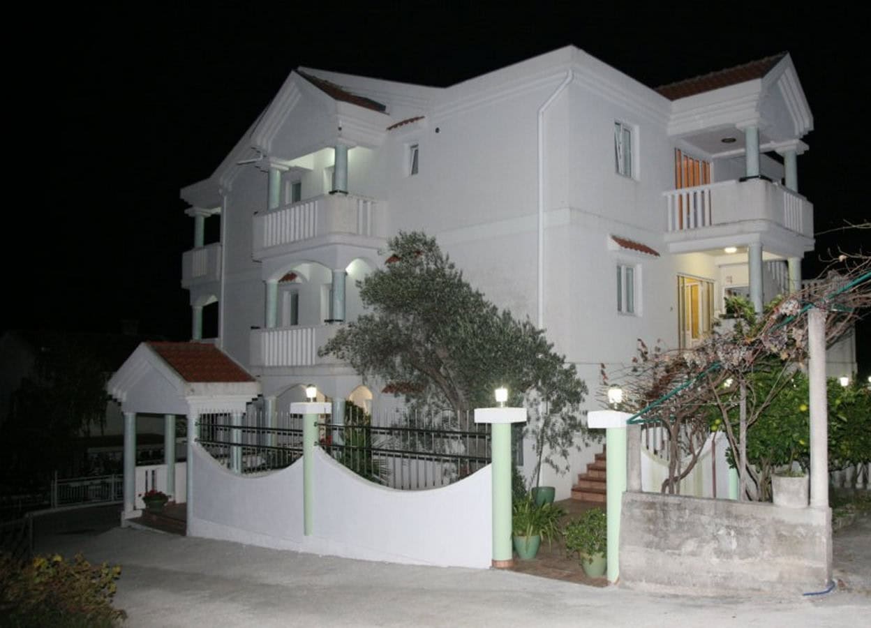 Dreistöckige Villa mit Balkonen und Terrasse in Tivat, Montenegro: Nachtansicht der beleuchteten Fassade mit Garten.