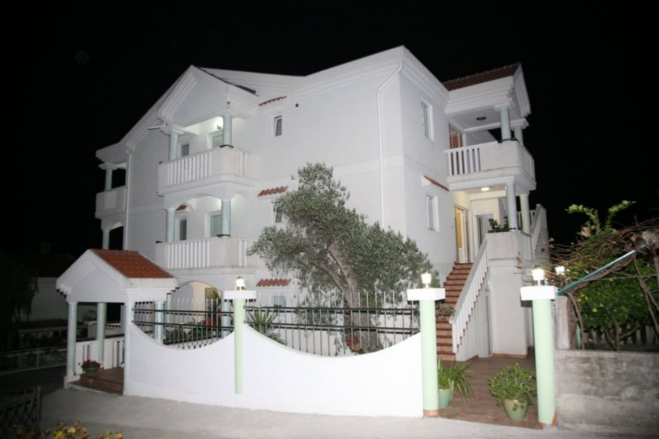 Dreistöckige weiße Villa in Tivat, Montenegro, mit Terrassen, Außentreppe und Zaun bei Nacht.