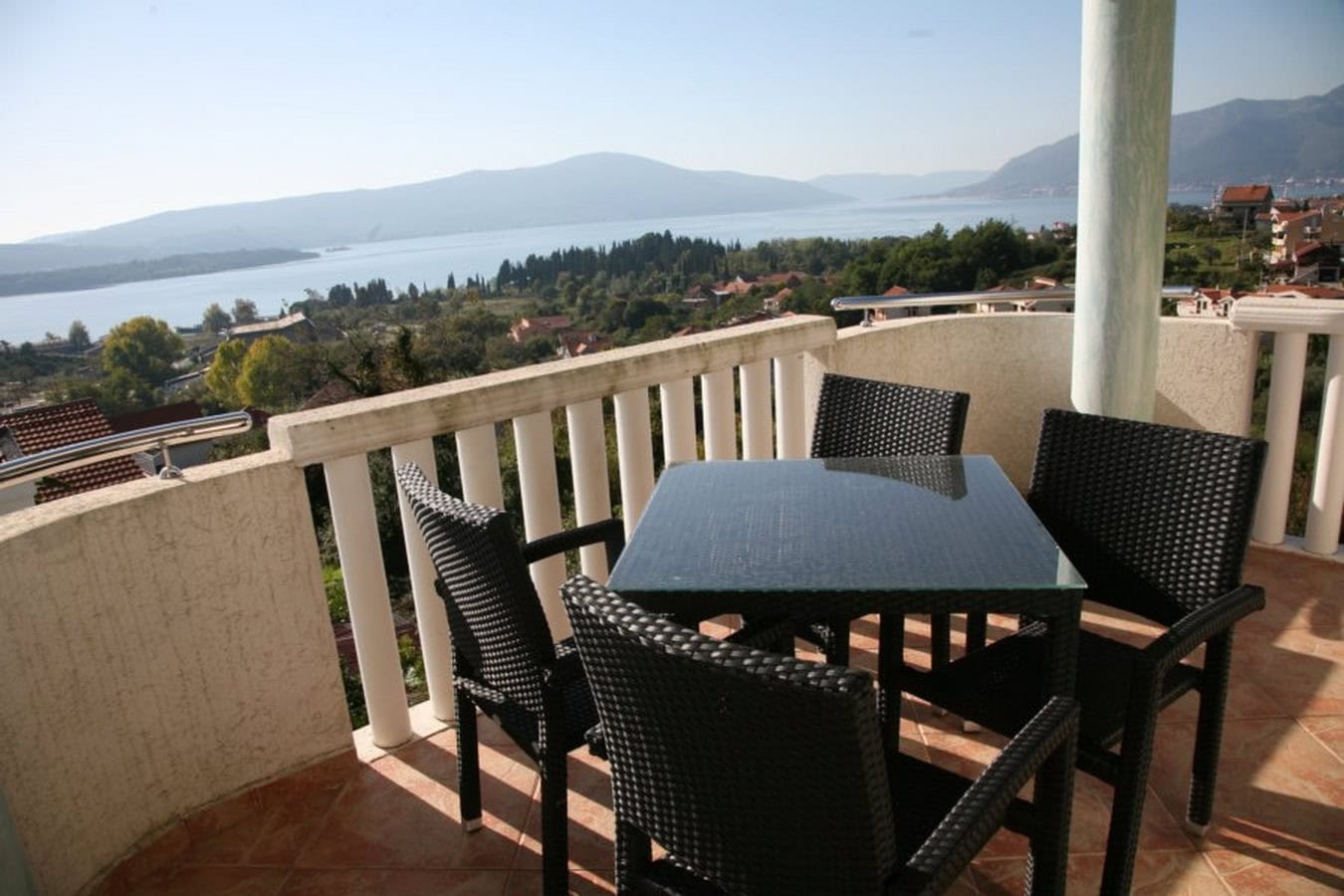 Terrasse der Villa in Tivat, Montenegro: geflochtene Möbel, Glastisch und Panoramablick auf die Bucht von Kotor und die Berge.