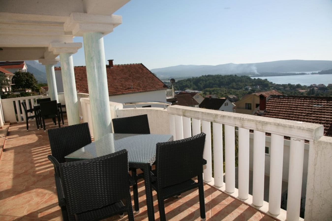 Terrasse der Villa in Tivat, Montenegro: geflochtene Stühle, Glastisch und Panoramablick auf das Meer und die Berge.
