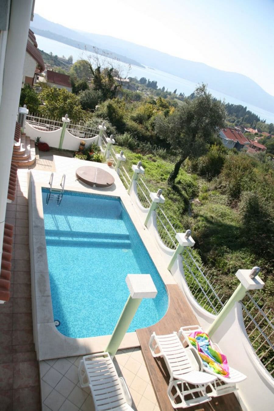 Offener Pool mit Blick auf das Meer und die Berge an der Villa in Tivat, Montenegro: Terrasse mit Liegestühlen und Landschaftsgestaltung.