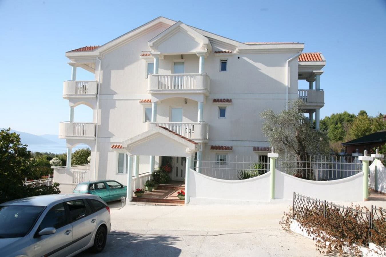 Dreistöckige Villa in Tivat, Montenegro: Fassade mit Balkonen, Parkplatz und Meerblick inmitten von Grün.