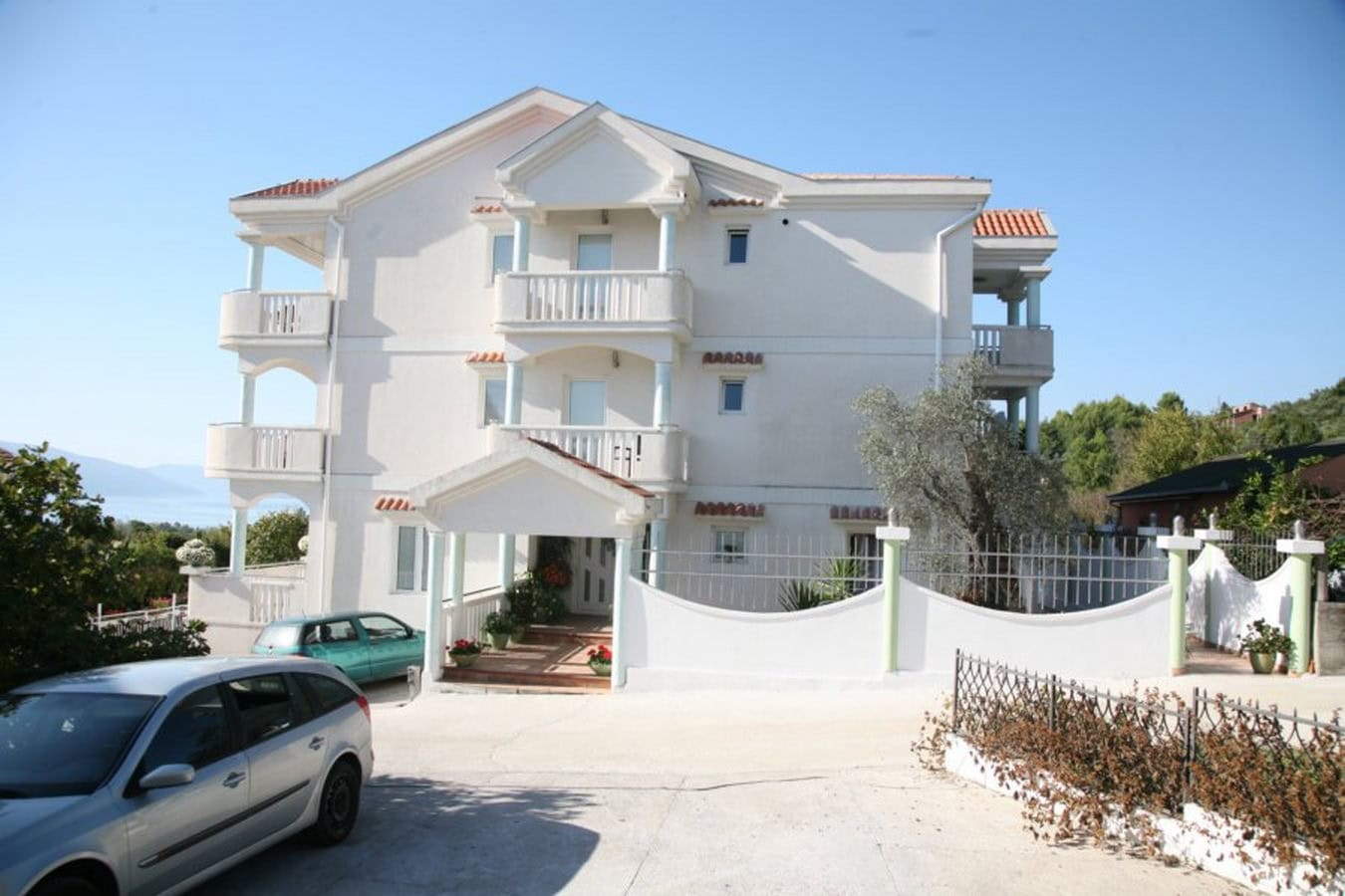 Dreistöckige weiße Villa mit Balkonen und Parkplatz in Tivat, Montenegro. Blick auf die Fassade des Hauses mit angrenzendem Grundstück.