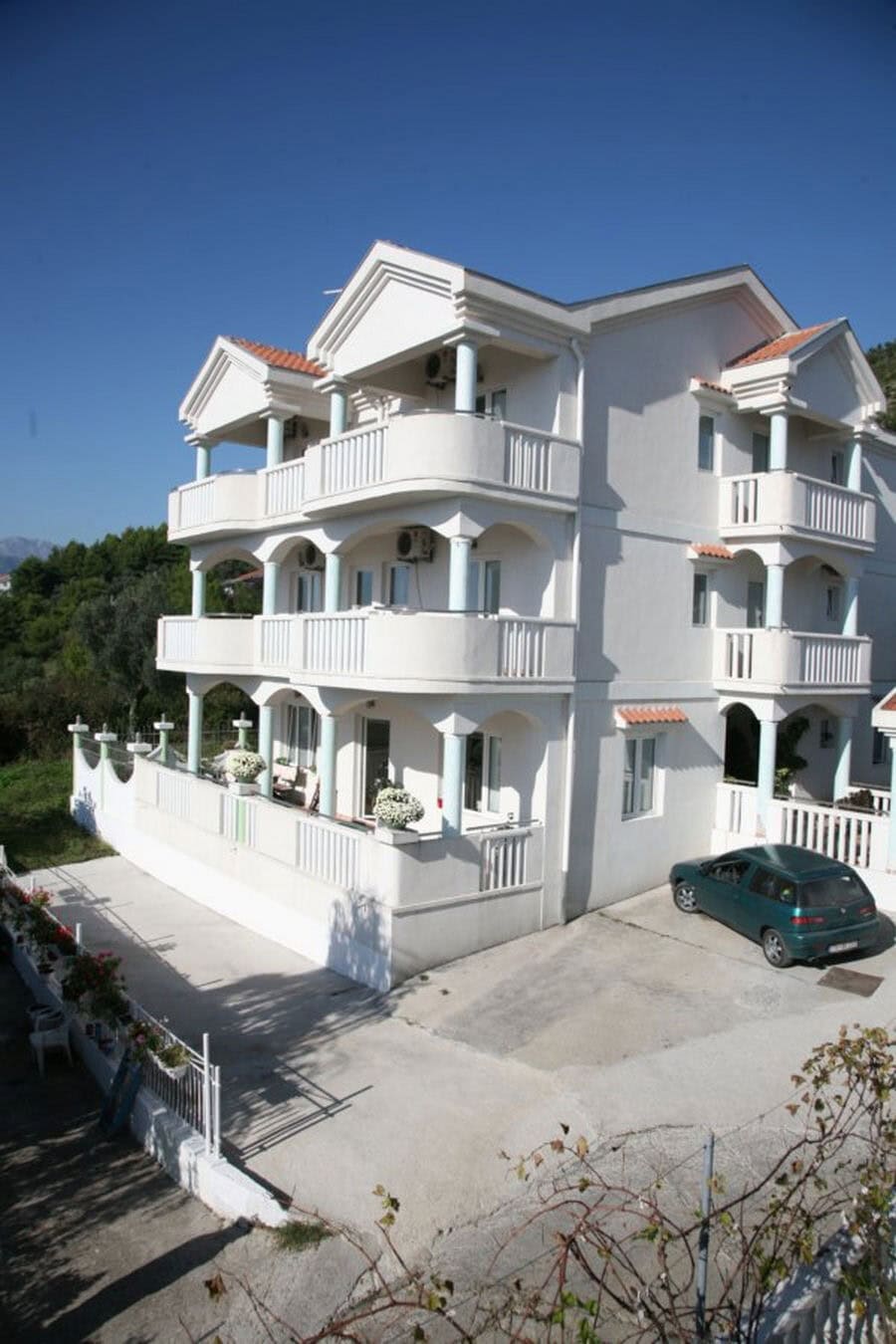 Dreistöckige weiße Villa in Tivat, Montenegro, mit offenen Terrassen, Säulen und Parkplätzen am Haus.