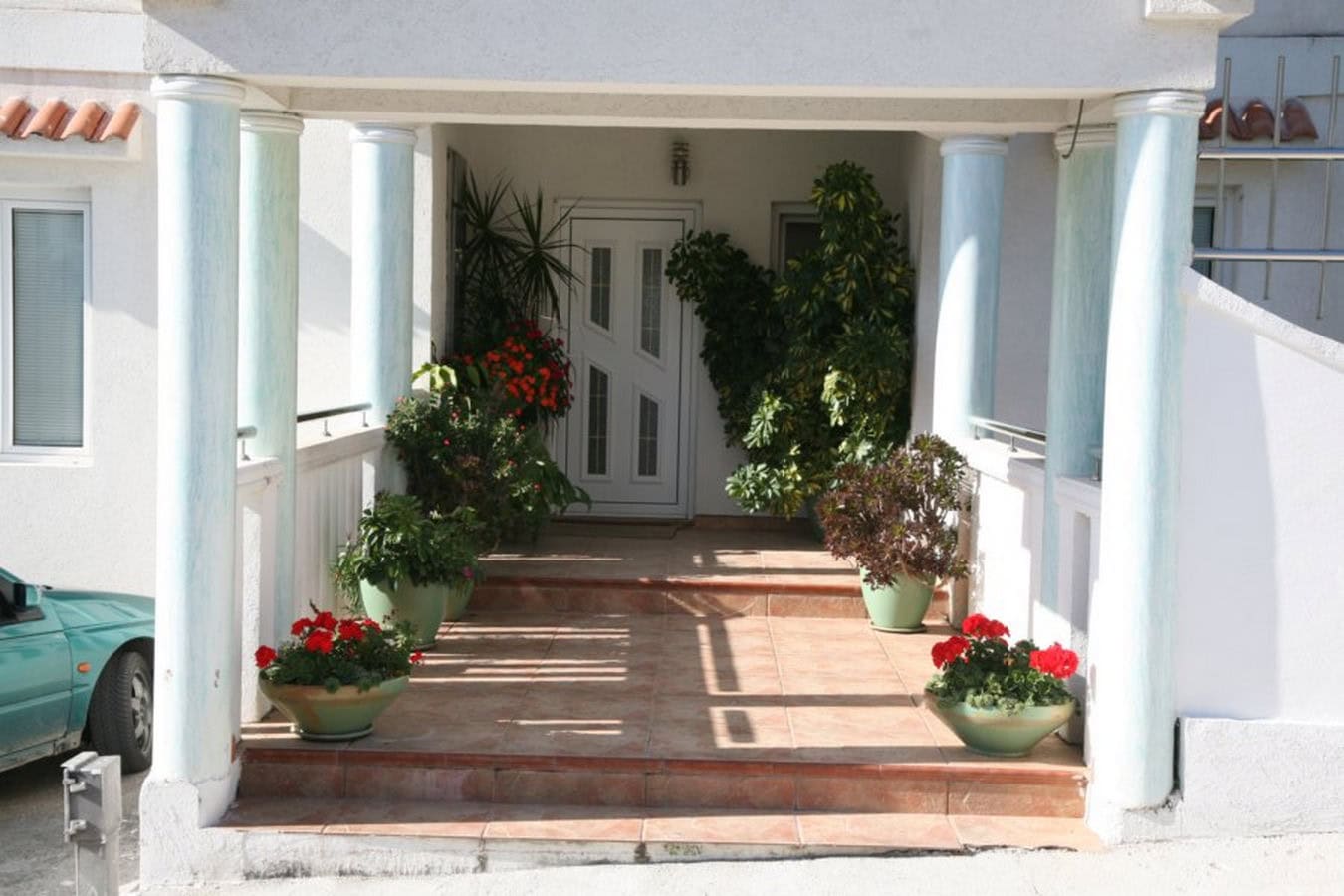 Eingang zur Villa in Tivat, Montenegro: Veranda mit Säulen, Terrakottafliesen und dekorativen Topfpflanzen.