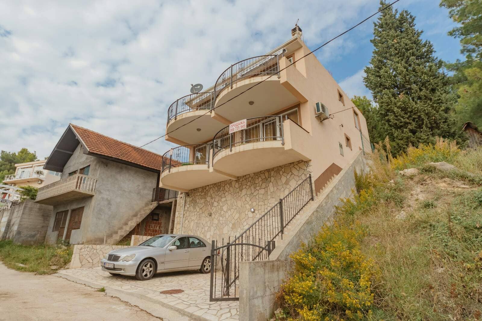 Трехэтажный дом с балконами и каменной отделкой фасада на продажу в Шушани, Черногория, с парковкой у входа.